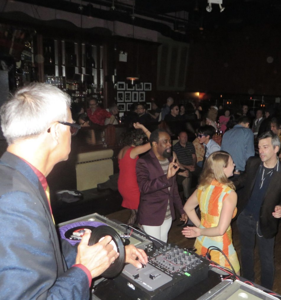 A DJ cueing a 45 on the decks while a crowd dances behind him at a Subway Soul Club night